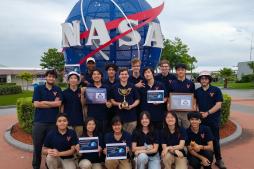 MARS team members, some holding awards, pose in front of the NASA sculpture at Kennedy Space Center